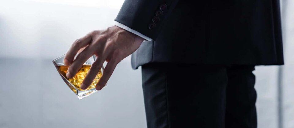 Hands holding a glass of whiskey in a suit, symbolizing alcohol addiction and recovery.