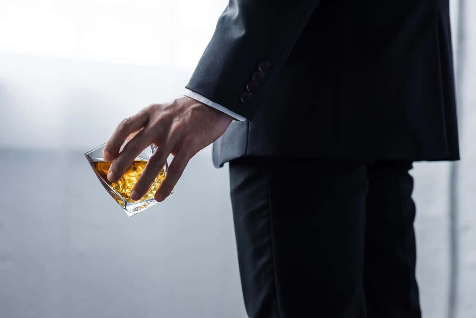 Hands holding a glass of whiskey in a suit, symbolizing alcohol addiction and recovery.