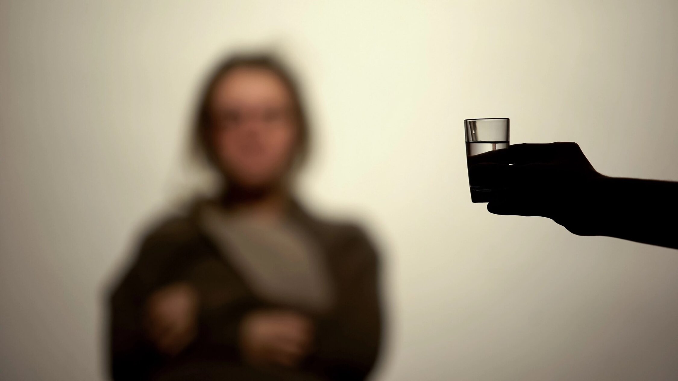 Empty shot glass of water held by a person silhouette, symbolizing sobriety and recovery. Focus on the glass for addiction recovery awareness.