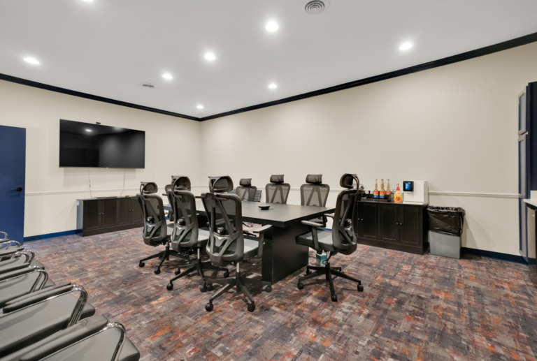 Modern conference room with black office chairs, large TV, and recovery-themed amenities.