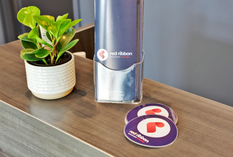 Brochure holder with Red Ribbon Recovery Indiana logo on a wooden reception desk.