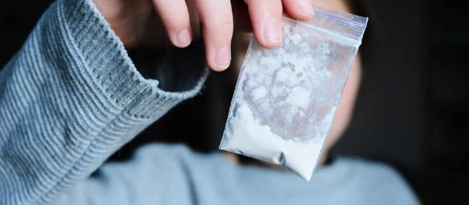 Powdered drug in a clear plastic bag held by a person in a gray sweater.