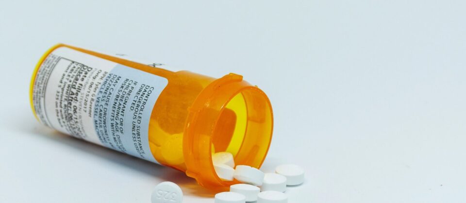 Prescribed medication pills spilling from a large orange pill bottle.