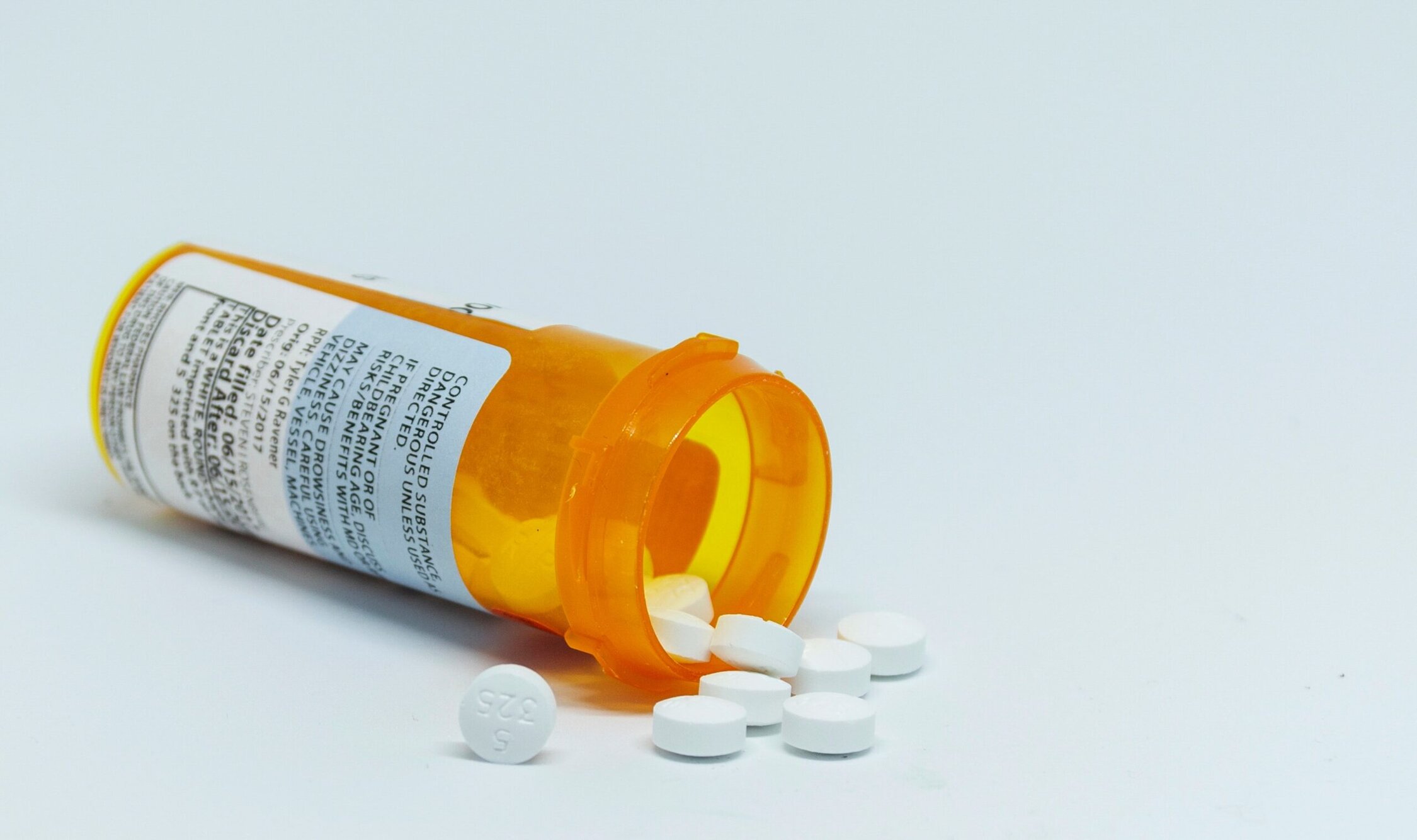 Prescribed medication pills spilling from a large orange pill bottle.