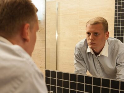 Reflective young man contemplating in bathroom mirror, seeking clarity and self-awareness.
