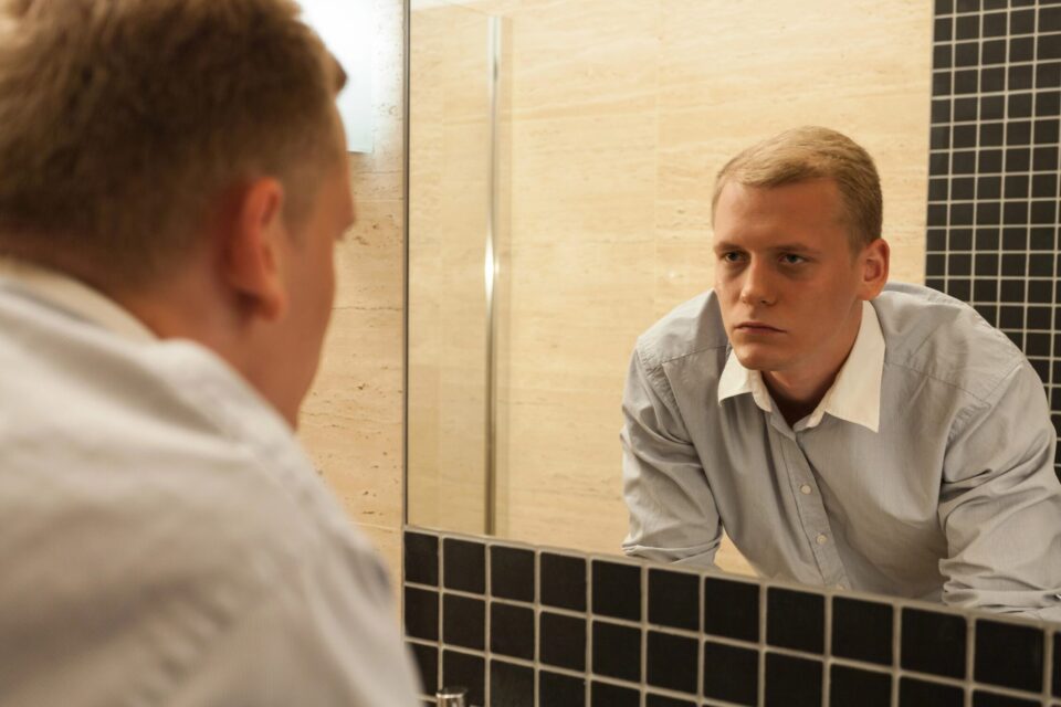 Reflective young man contemplating in bathroom mirror, seeking clarity and self-awareness.