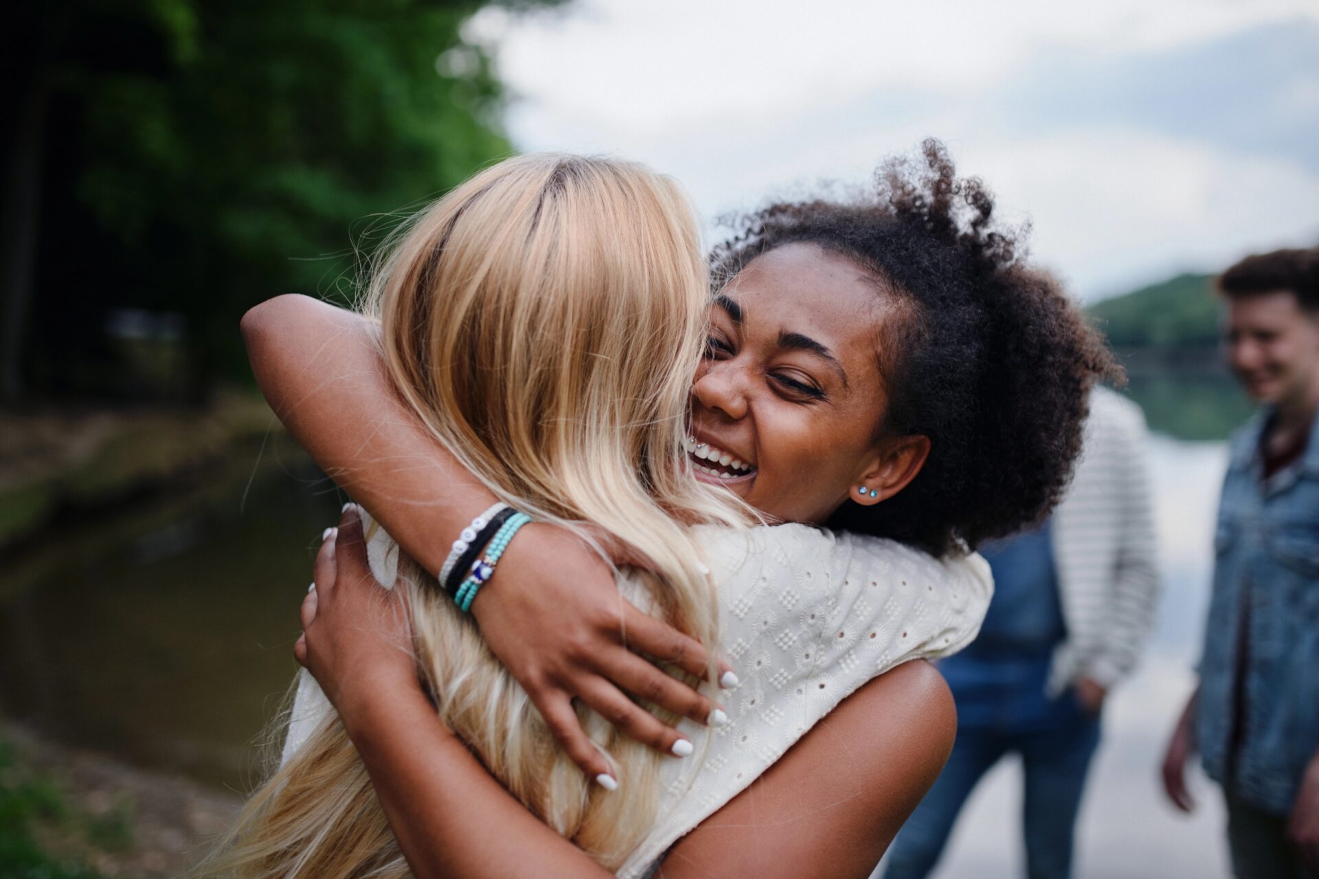 Two women embracing outdoors near water, smiling and happy.