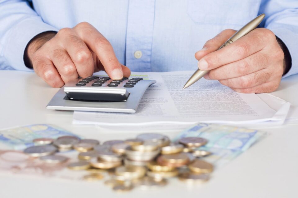 Person calculating finances with calculator and coins for recovery planning.