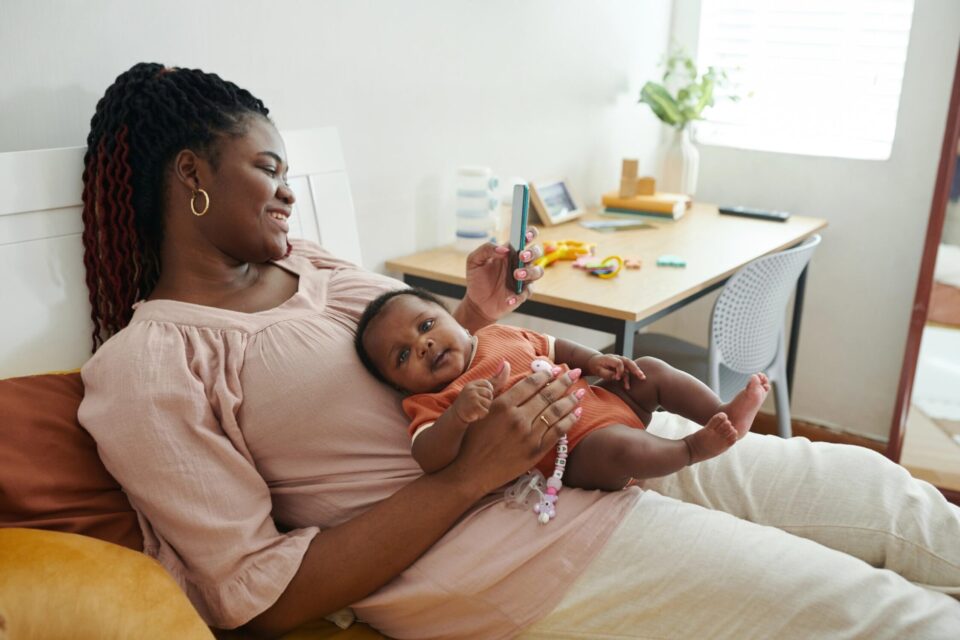 Mother and baby relaxing together, mother using smartphone, cozy home setting.
