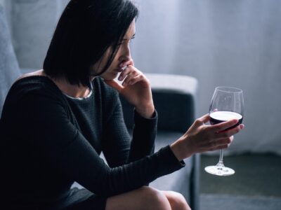 Contemplative woman holding a glass of red wine, reflecting on sobriety and recovery.