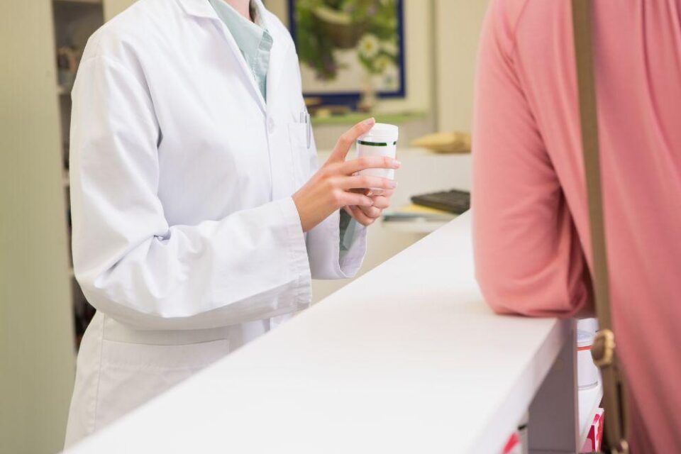 Nurse handing medication to patient at clinic reception desk.