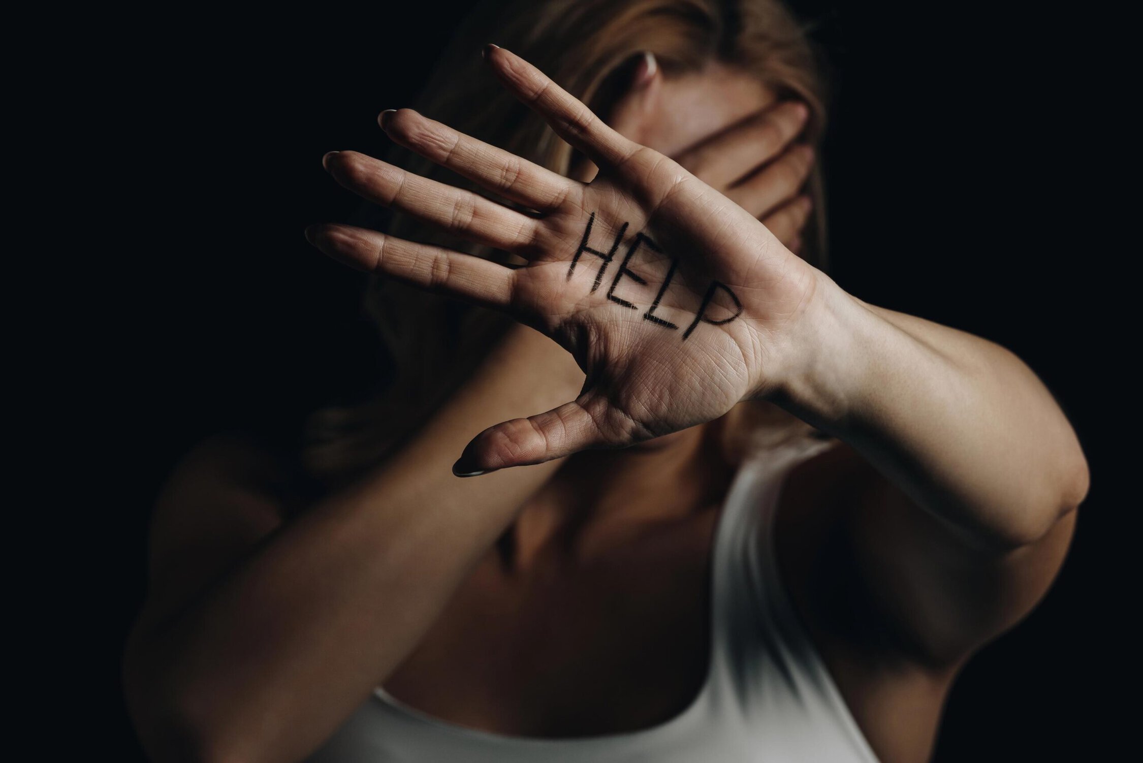 Help sign written on palm of woman with face partially covered, emphasizing mental health awareness.