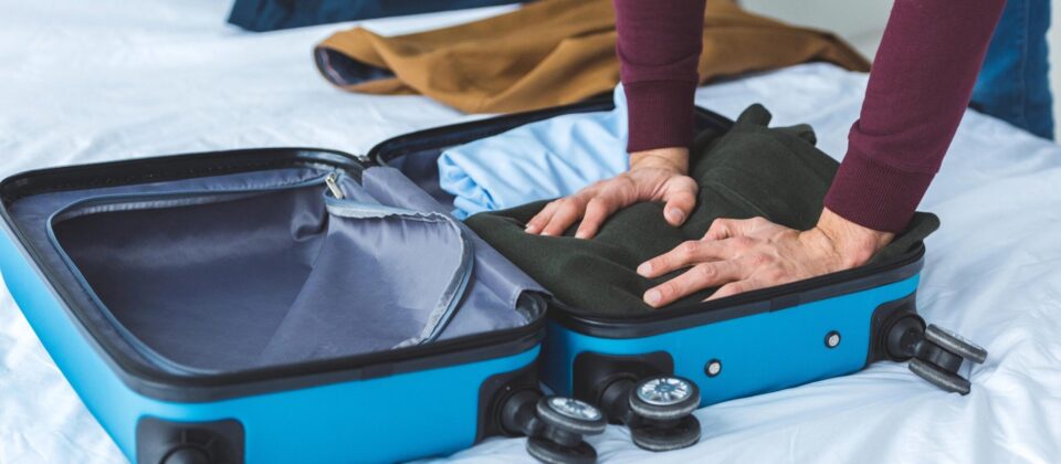 Empty blue suitcase being packed with clothes on a bed.