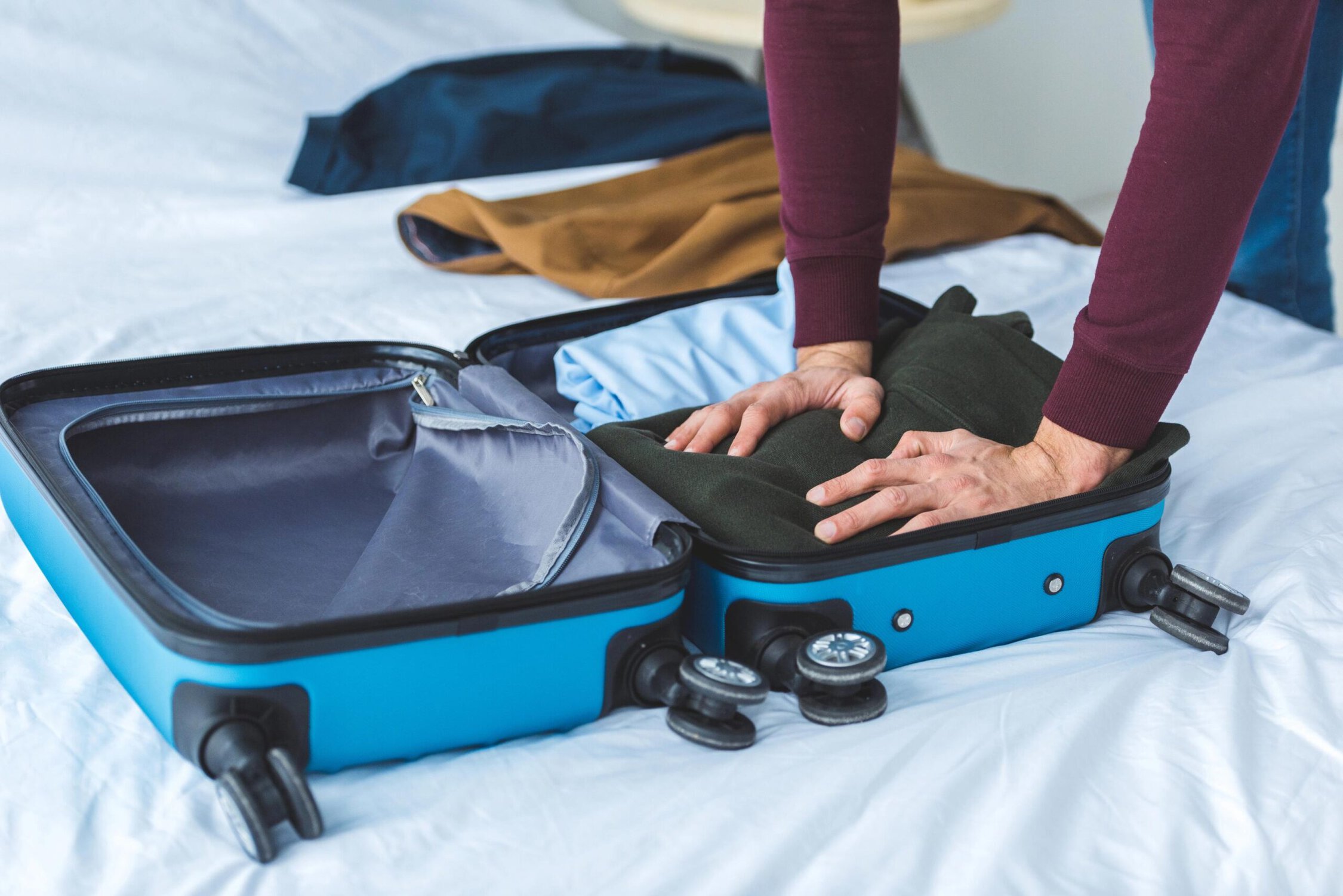 Empty blue suitcase being packed with clothes on a bed.